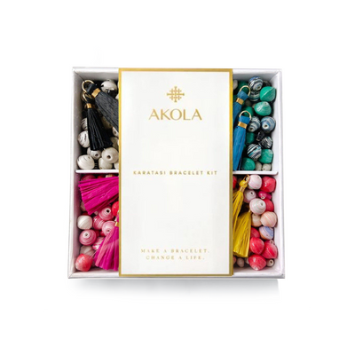 A boxed DIY bracelet kit by Akola, featuring various colorful hand-rolled beads and raffia tassels.